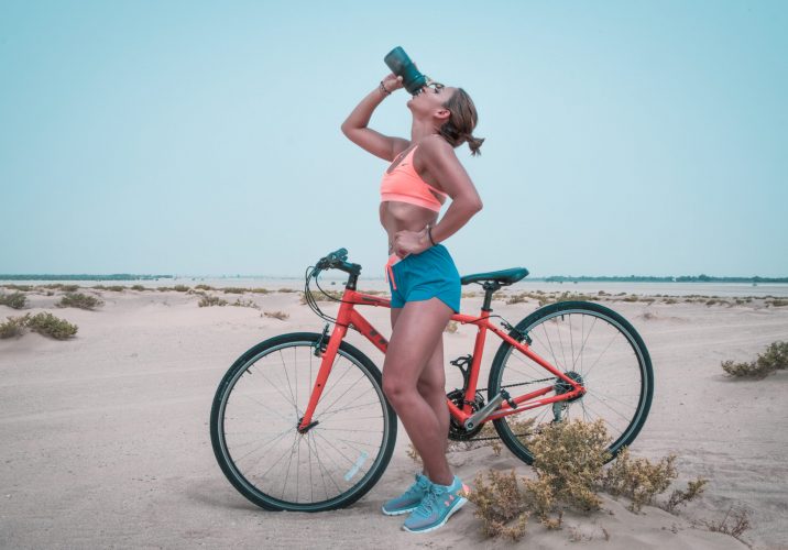 Woman drinking on black tumbler while looking up and placing her left hand on waist